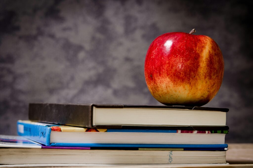 Red apple placed atop stacked books symbolizes education and learning.
