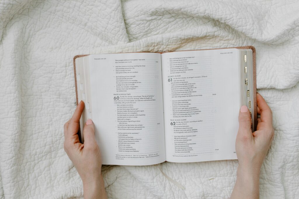 Open Bible held by hands on a white quilted fabric, perfect for religious themes.